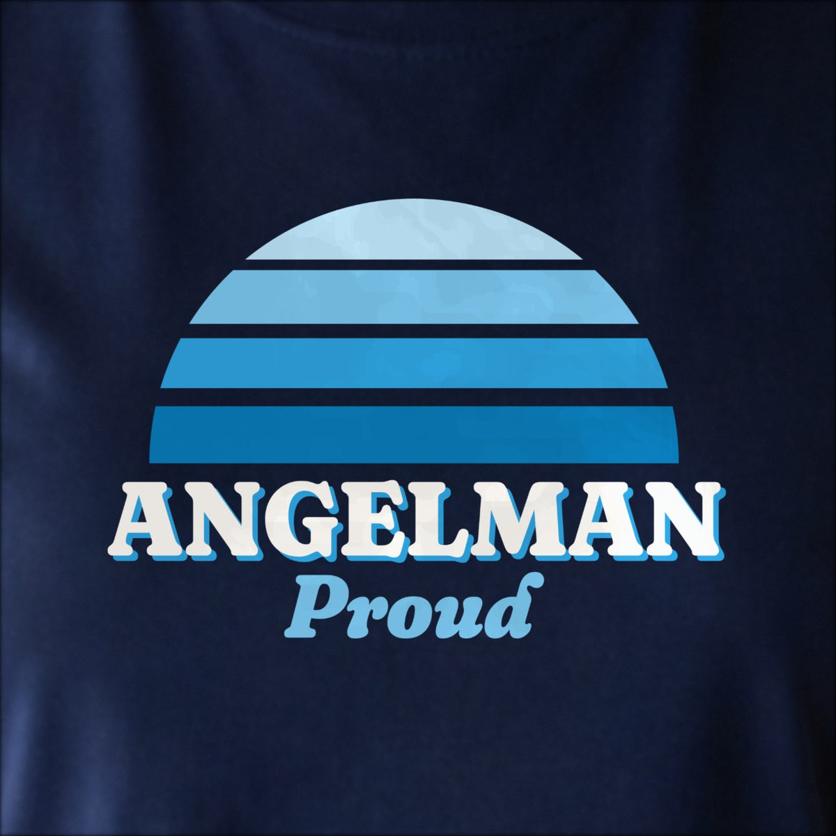 Close-up of the print on navy: a striped half-sun in blue above cream ANGELMAN lettering with “Proud” in script.