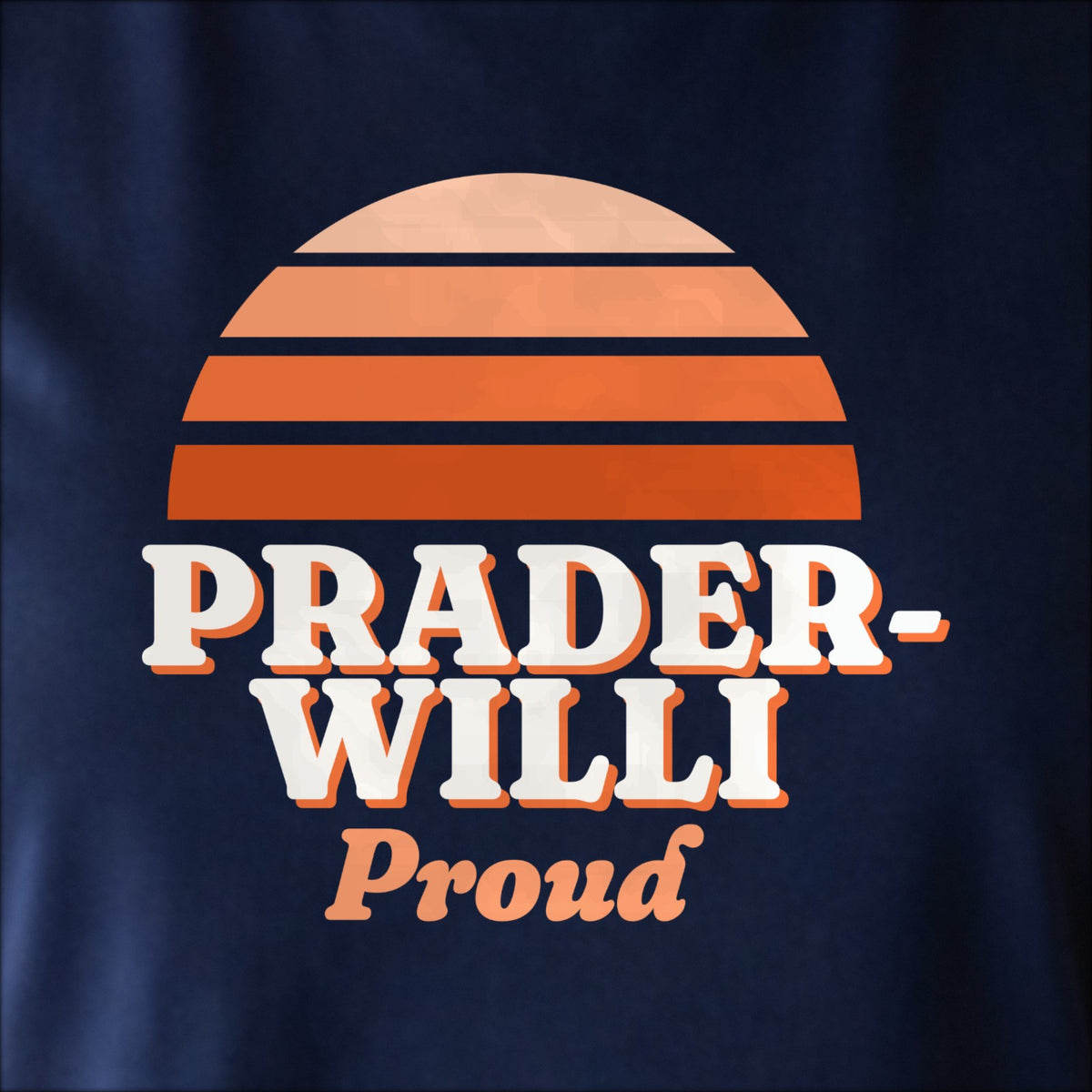 Close-up of the print on navy: a striped half-sun in orange above cream PRADER-WILLI lettering with “Proud” in script.