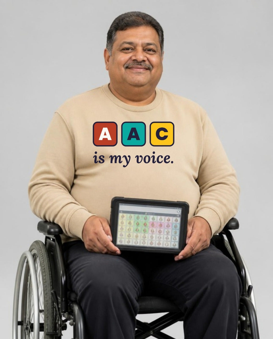 Man who uses a wheelchair holding his AAC talker, wearing the AAC Is My Voice Adult Sweatshirt in Sand