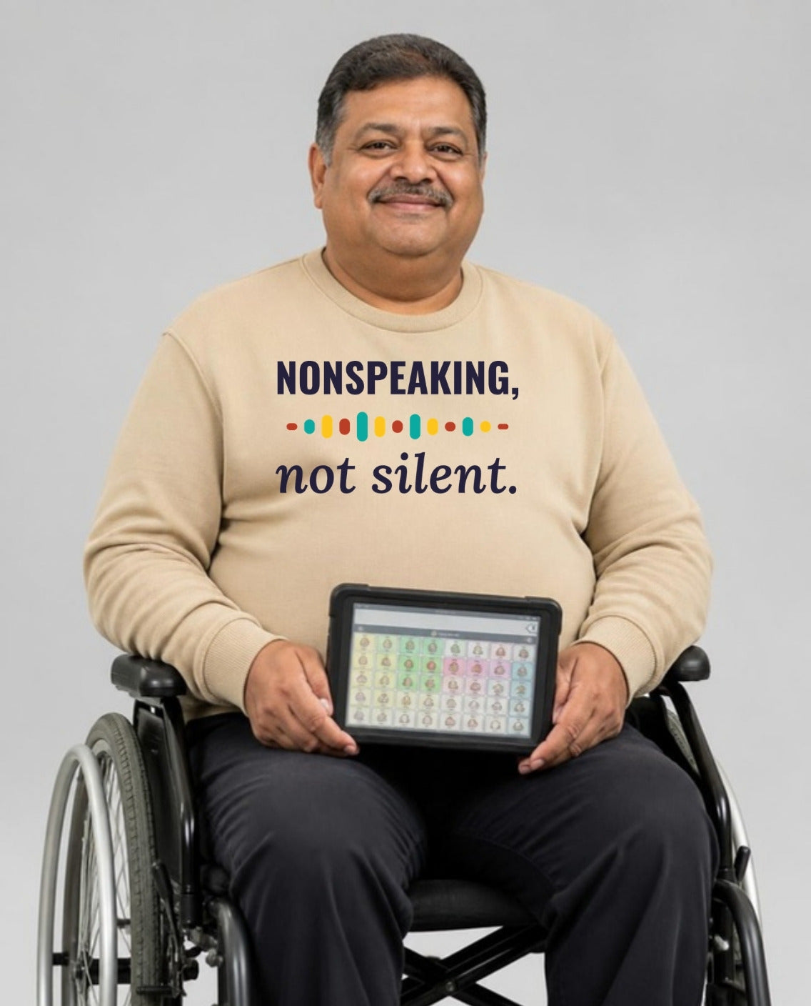Man who uses a wheelchair holding his AAC talker, wearing the Nonspeaking, Not Silent Adult Sweatshirt in Sand