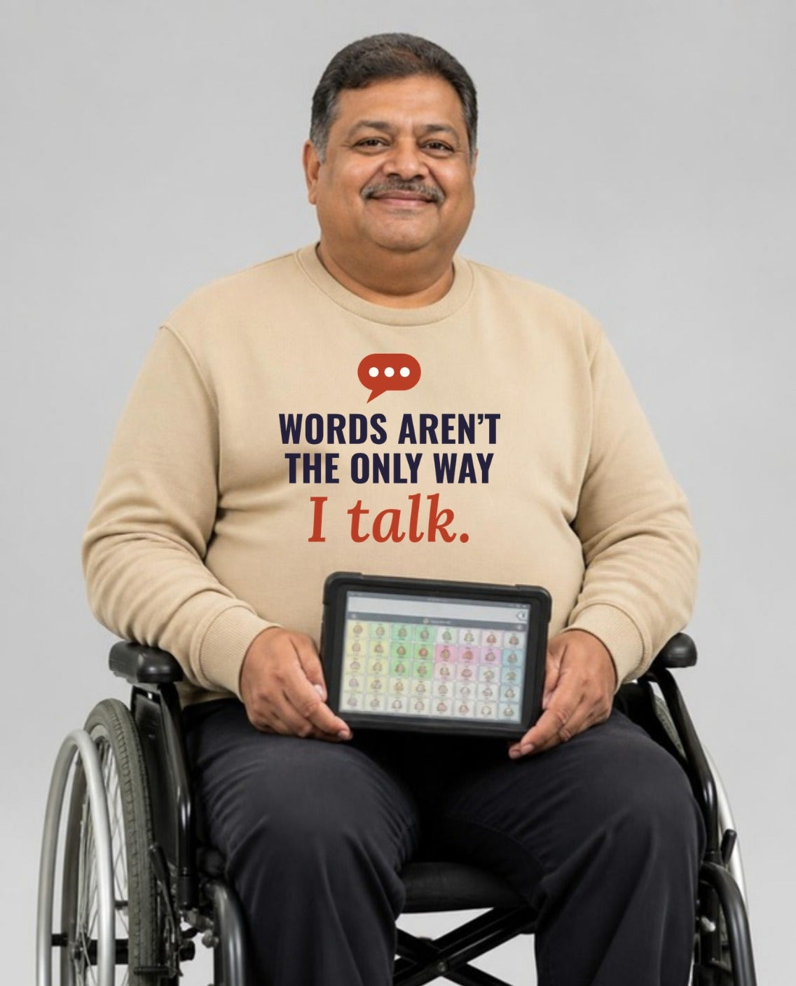 Man who uses a wheelchair holding his AAC talker, wearing the Words Aren’t the Only Way I Talk Adult Sweatshirt in Sand