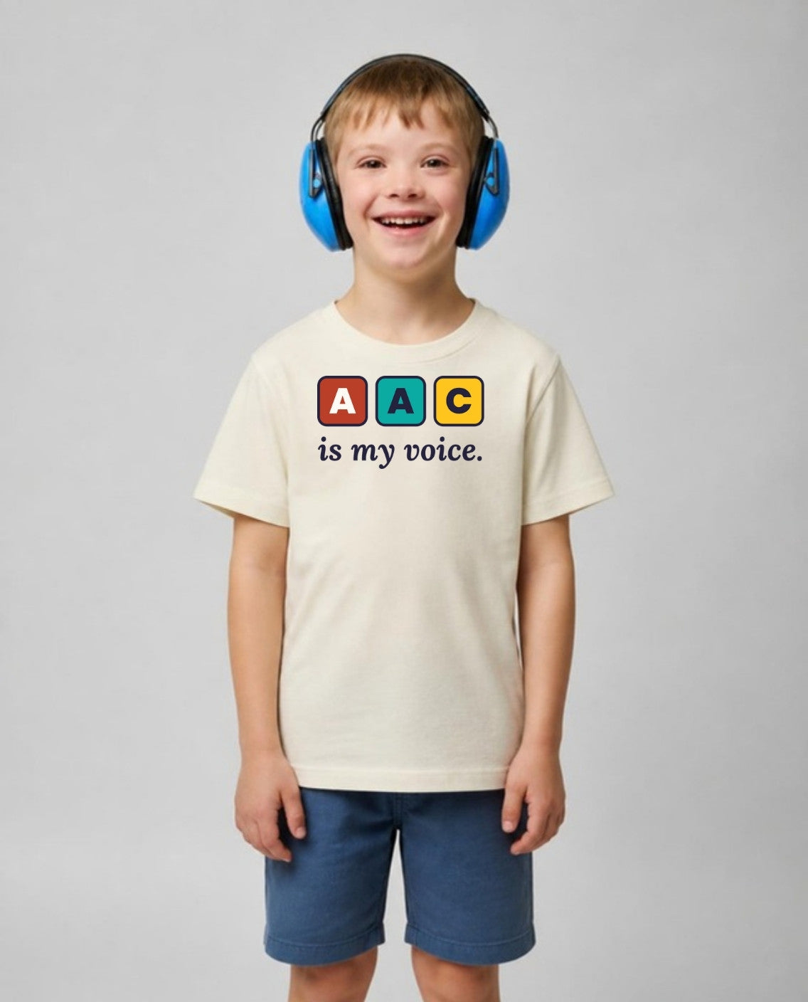 Boy with Down syndrome in noise-blocking headphones wearing the AAC Is My Voice Youth Tee in Natural