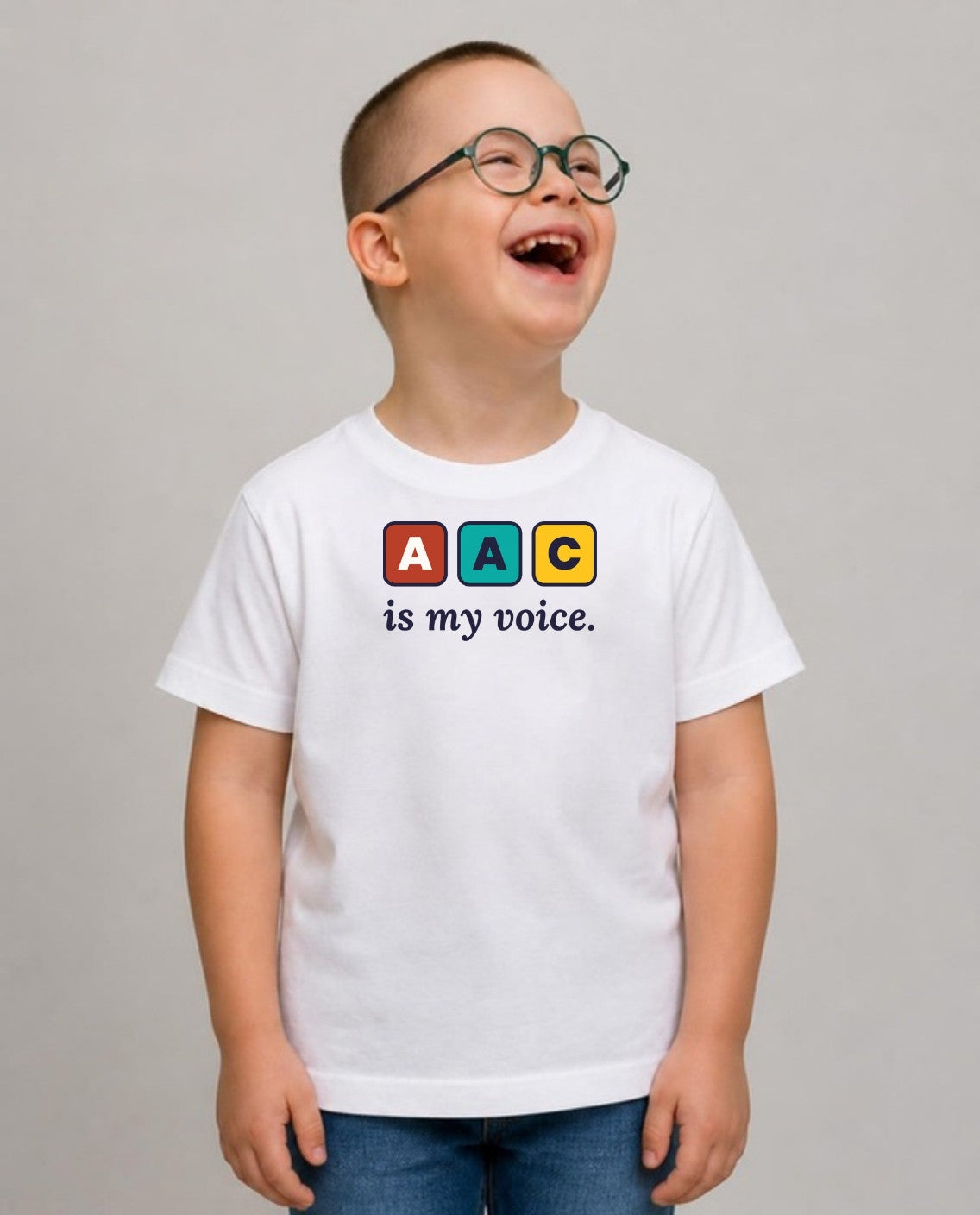 Boy in glasses laughing, looking up and away, wearing the AAC Is My Voice Youth Tee in White