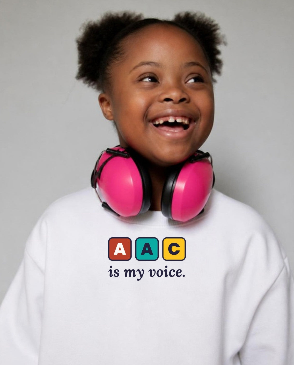 Girl with Down syndrome laughing, headphones around her neck, wearing the AAC Is My Voice Youth Sweatshirt in White