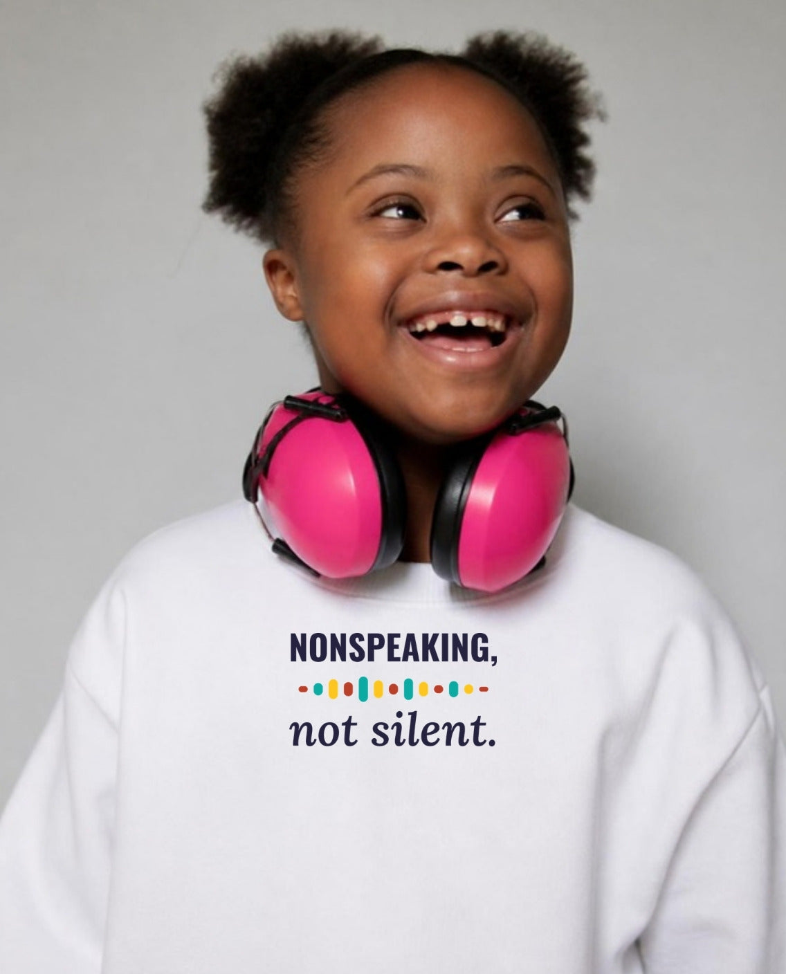 Girl with Down syndrome laughing, headphones around her neck, wearing the Nonspeaking, Not Silent Youth Sweatshirt in White