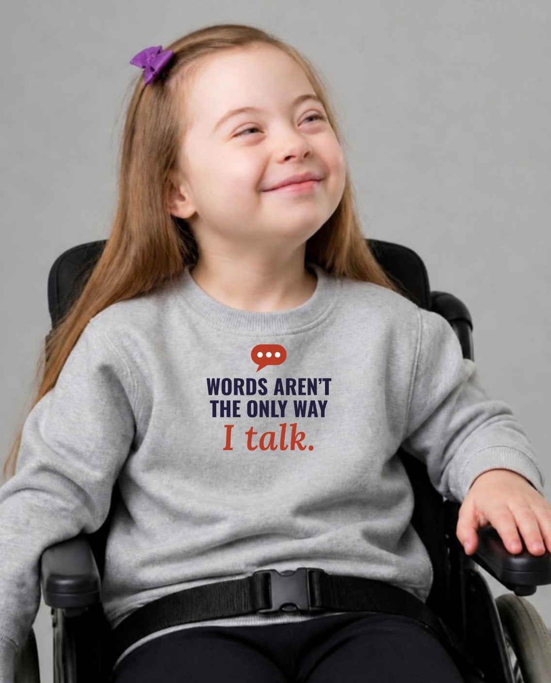Girl in her wheelchair smiling softly wearing the Words Aren’t the Only Way I Talk Youth Sweatshirt in Sport Grey