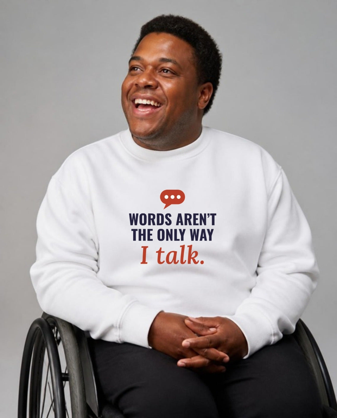 Man in his wheelchair smiling, looking up and away, wearing the Words Aren’t the Only Way I Talk Adult Sweatshirt in White