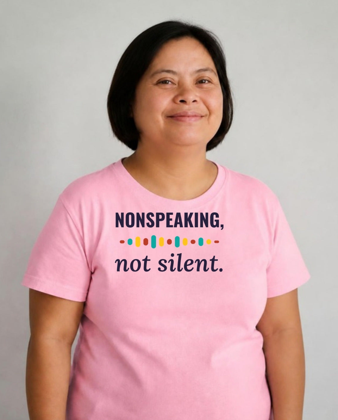 Woman with Down syndrome smiling calmly wearing the Nonspeaking, Not Silent Adult Tee in Pink