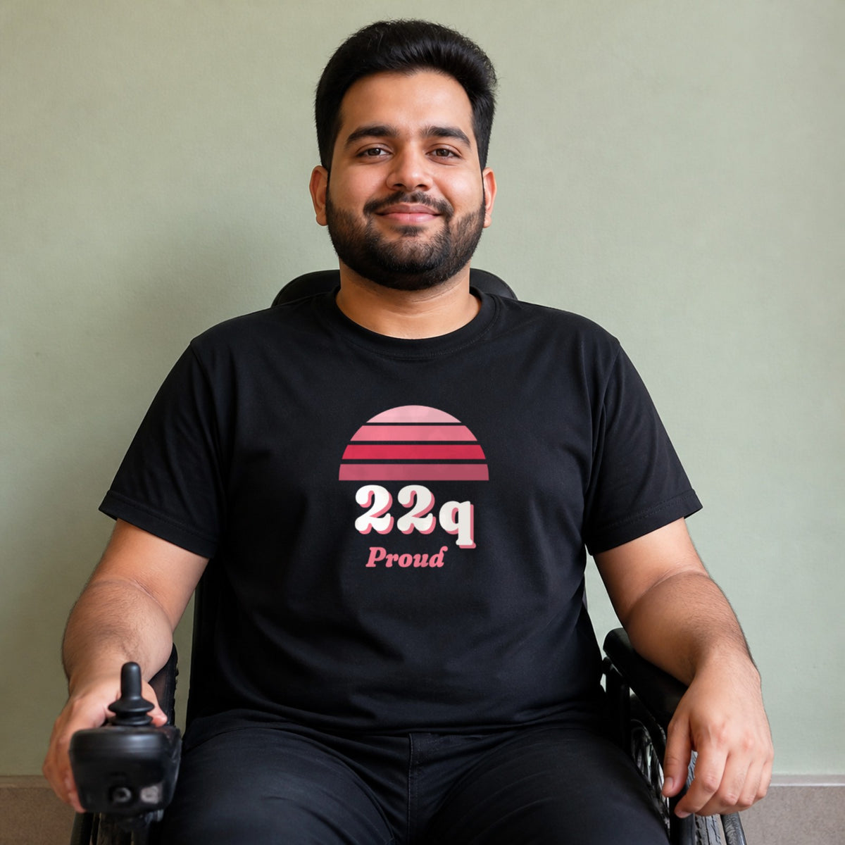 A man seated in a power wheelchair wears a black 22q Proud tee.