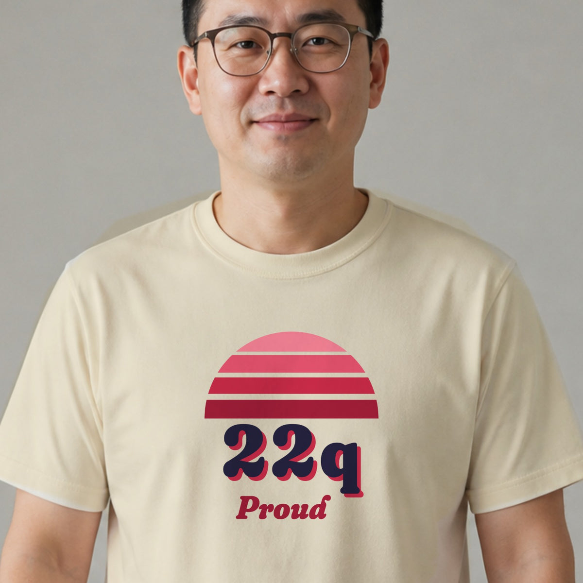 A man in glasses wears a natural-colored 22q Proud tee with a red striped retro sun.