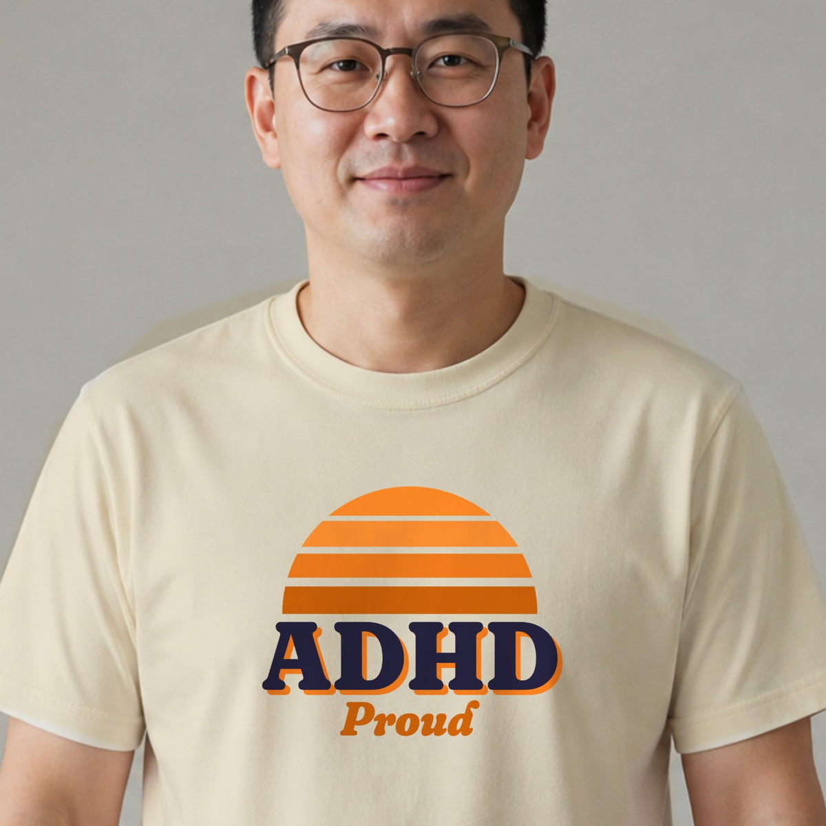 A man in glasses wears a natural-colored ADHD Proud tee with an orange striped retro sun.