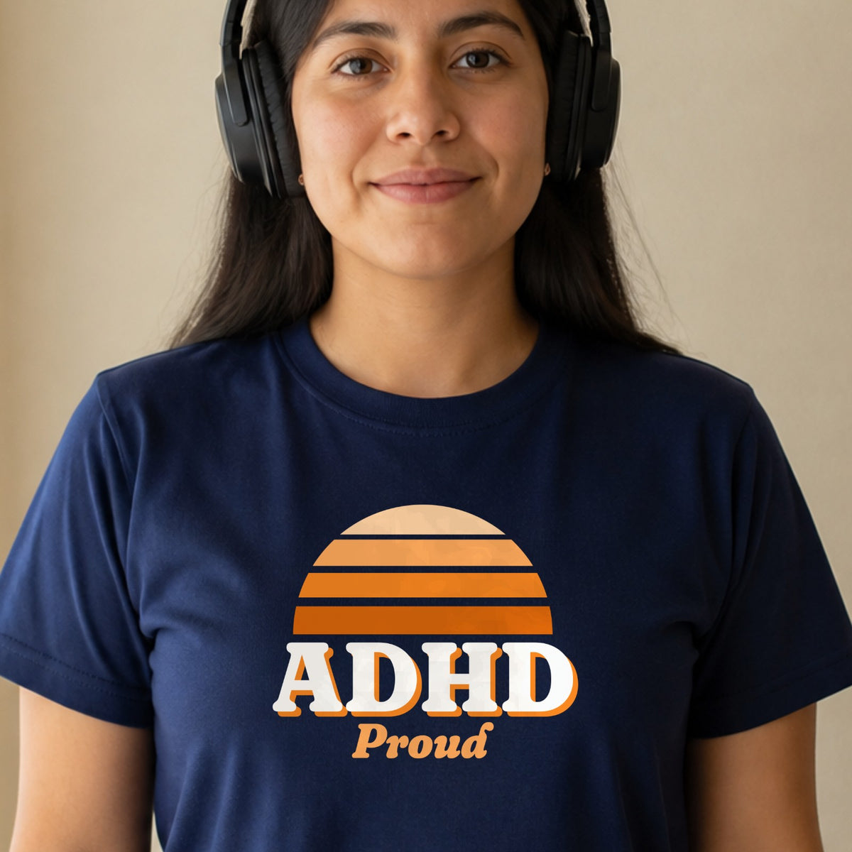 A woman in over-ear headphones wears a navy ADHD Proud tee with an orange striped retro sun.