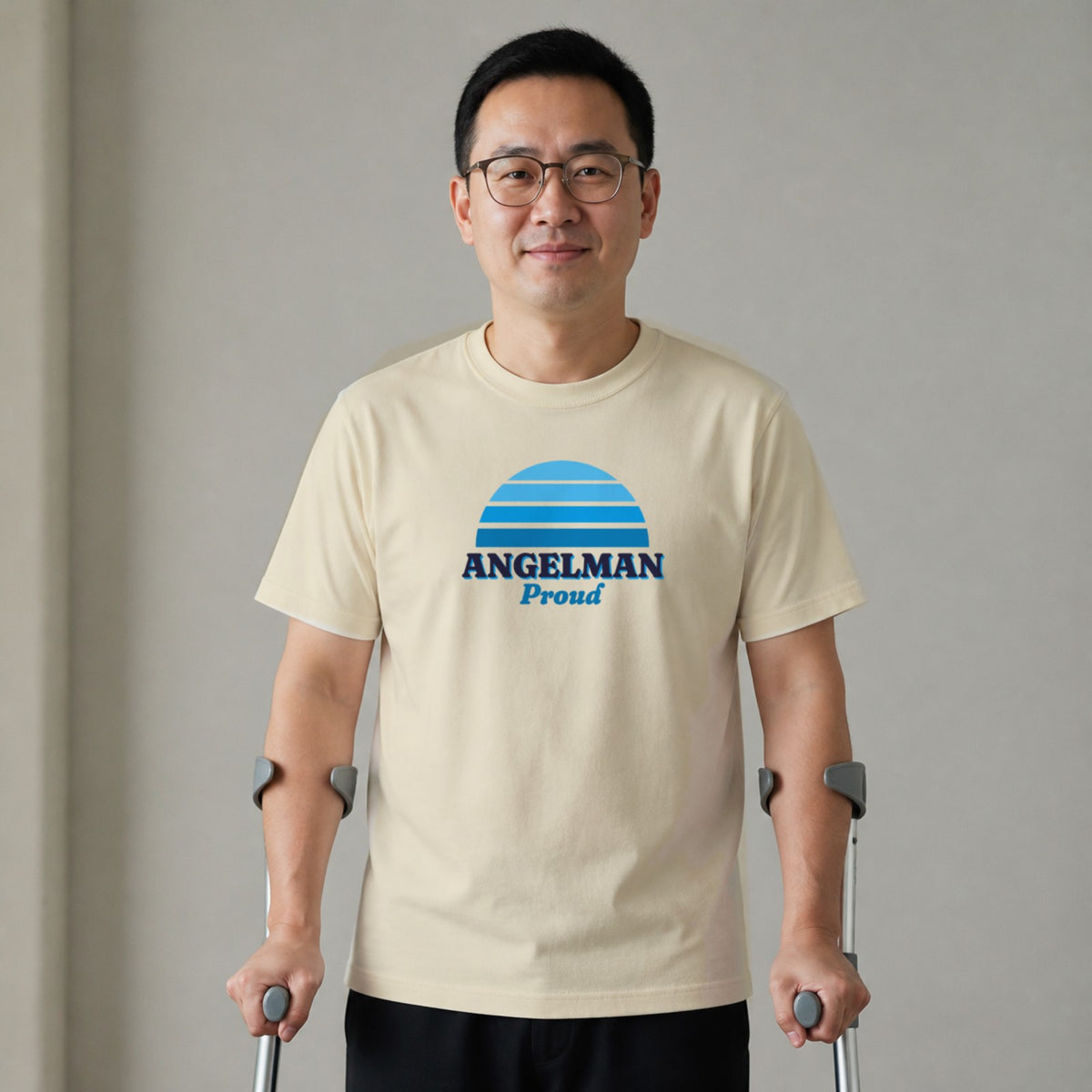 A man standing with two forearm crutches wears a natural-colored Angelman Proud tee.