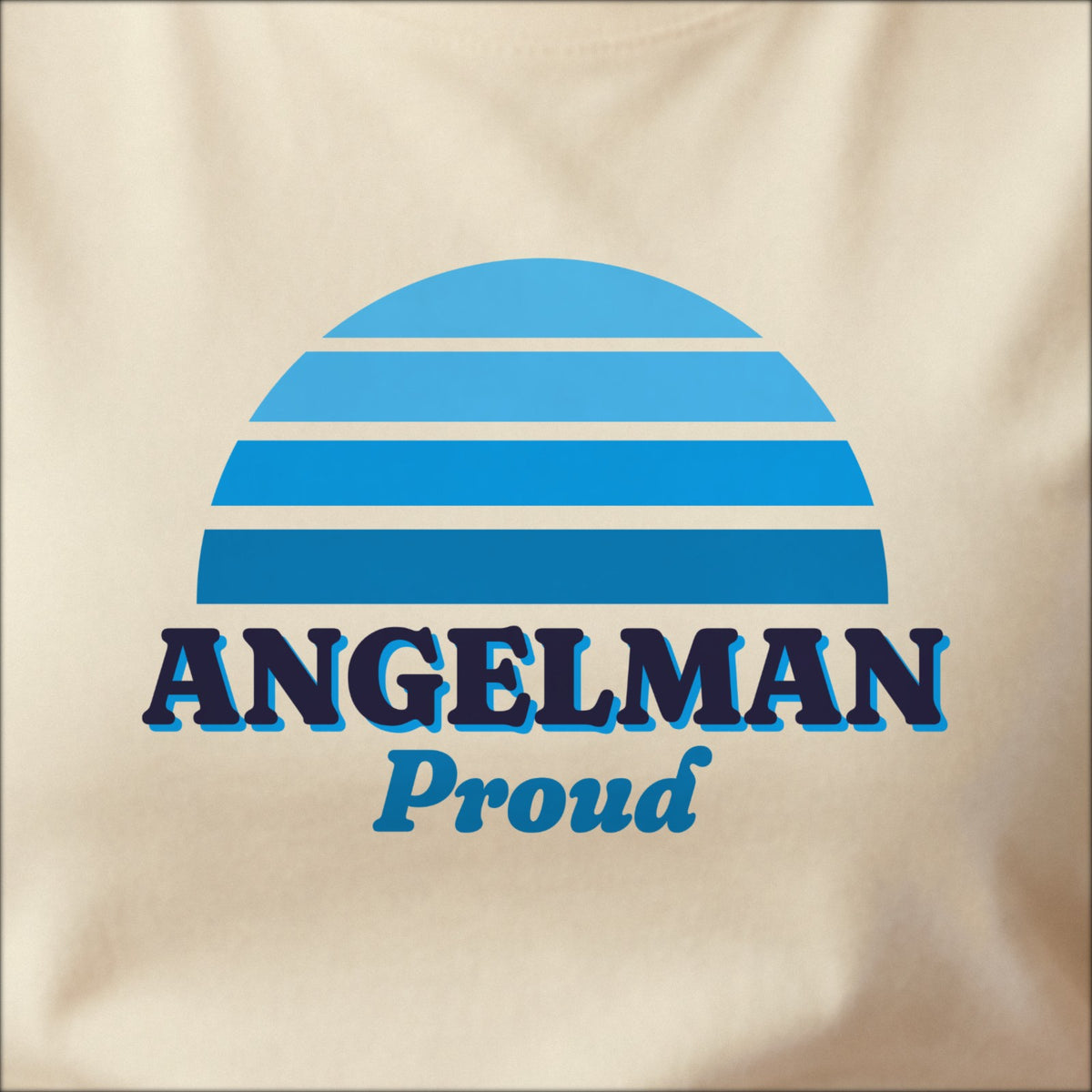 Close-up of the print on a natural tee: a striped half-sun in blue above bold ANGELMAN lettering with “Proud” in script.