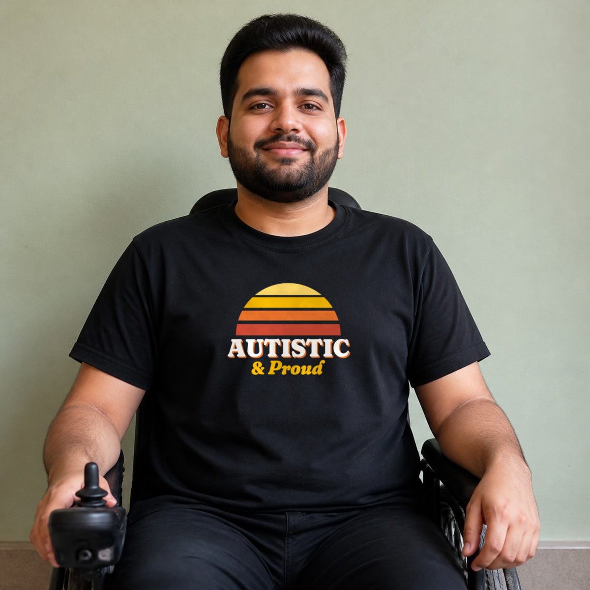 A man seated in a power wheelchair wears a black Autistic & Proud tee.