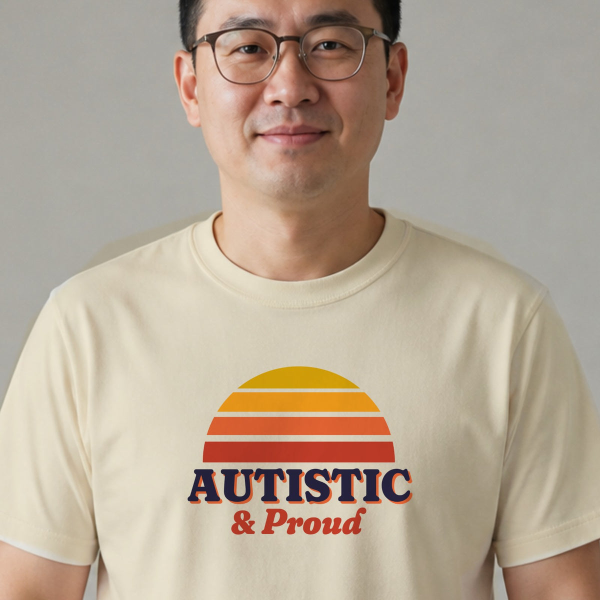 A man in glasses wears a natural-colored Autistic & Proud tee with a gold and red striped retro sun.