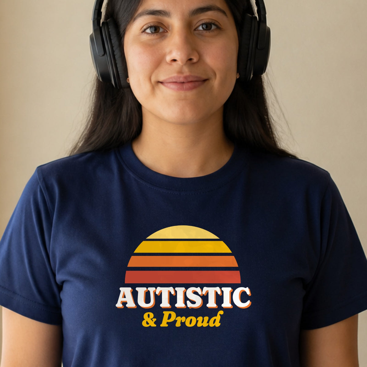 A woman in over-ear headphones wears a navy Autistic & Proud tee with a gold and red striped retro sun.