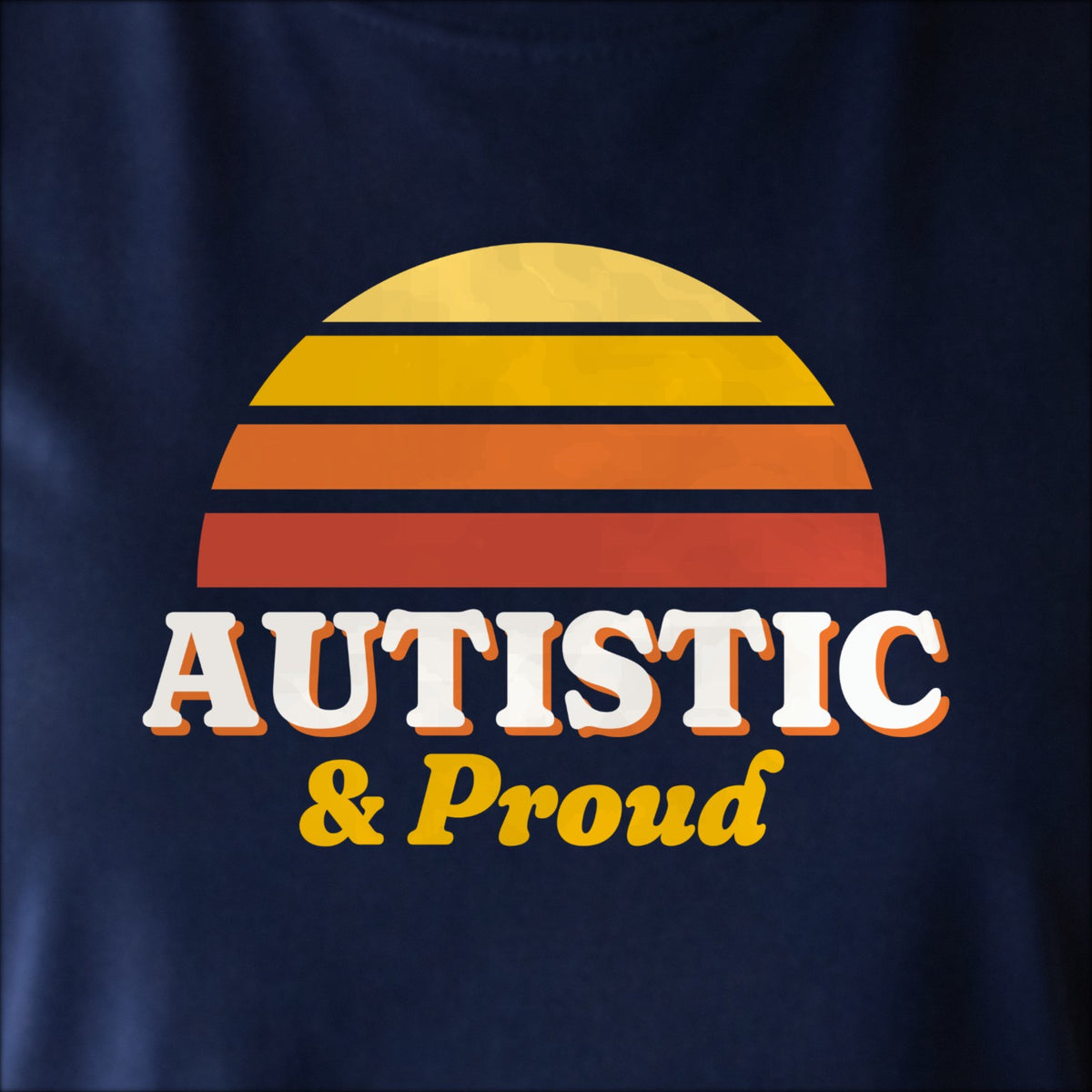 Close-up of the print on navy: a striped half-sun in gold and red above cream AUTISTIC lettering with “& Proud” in script.