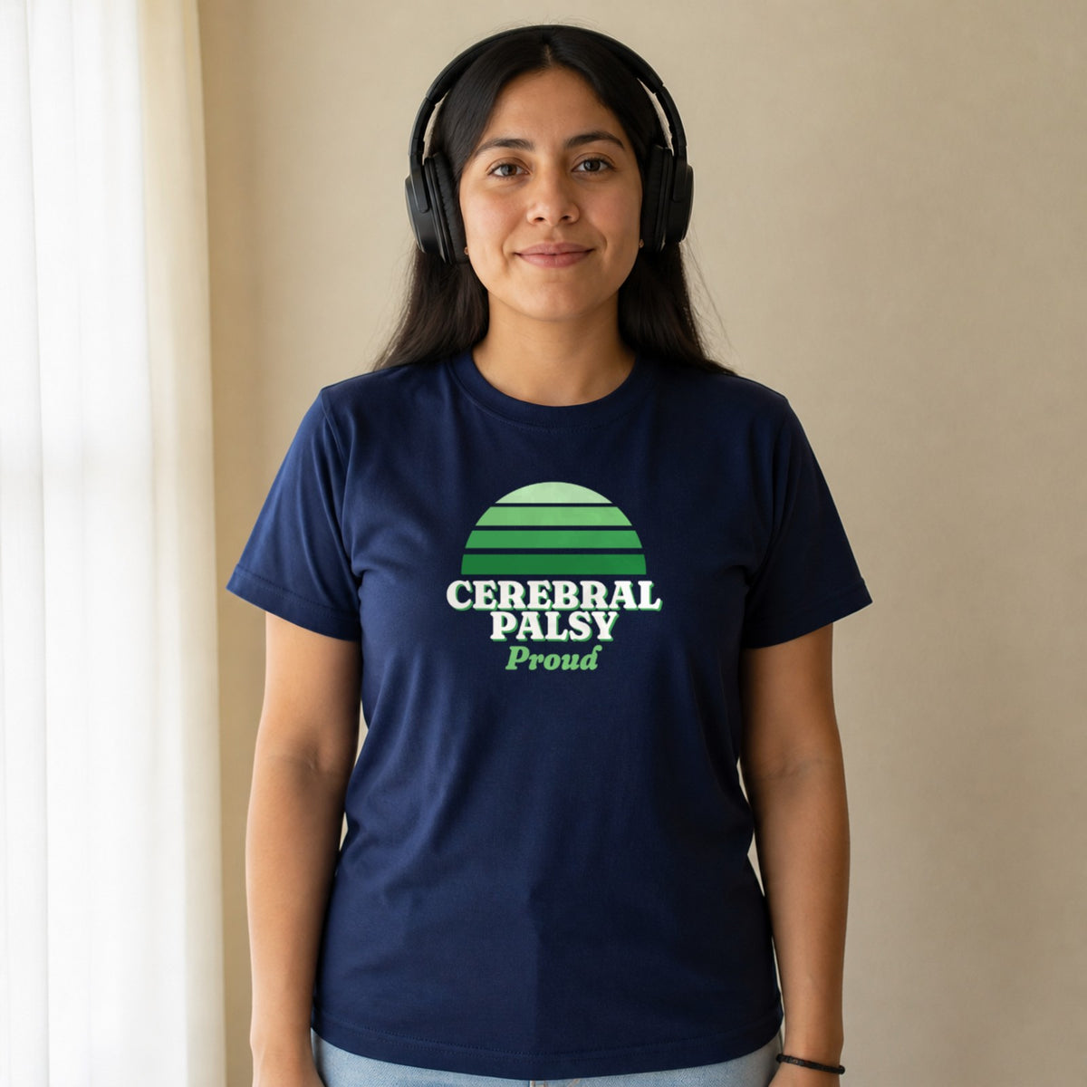 A woman in over-ear headphones wears a navy Cerebral Palsy Proud tee.