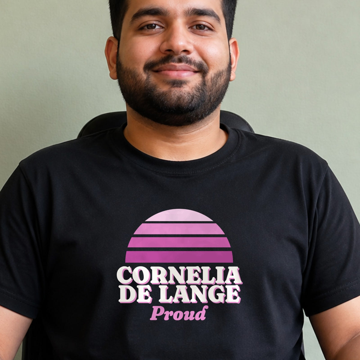A man wears a black Cornelia de Lange Proud tee with a purple striped retro sun.