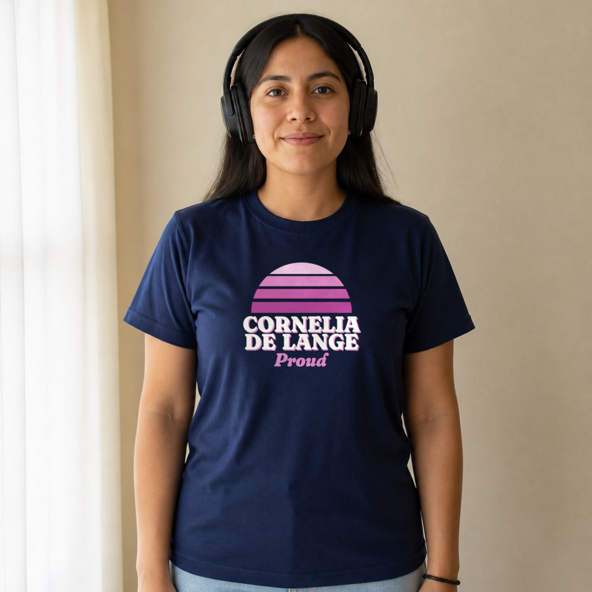 A woman in over-ear headphones wears a navy Cornelia de Lange Proud tee.