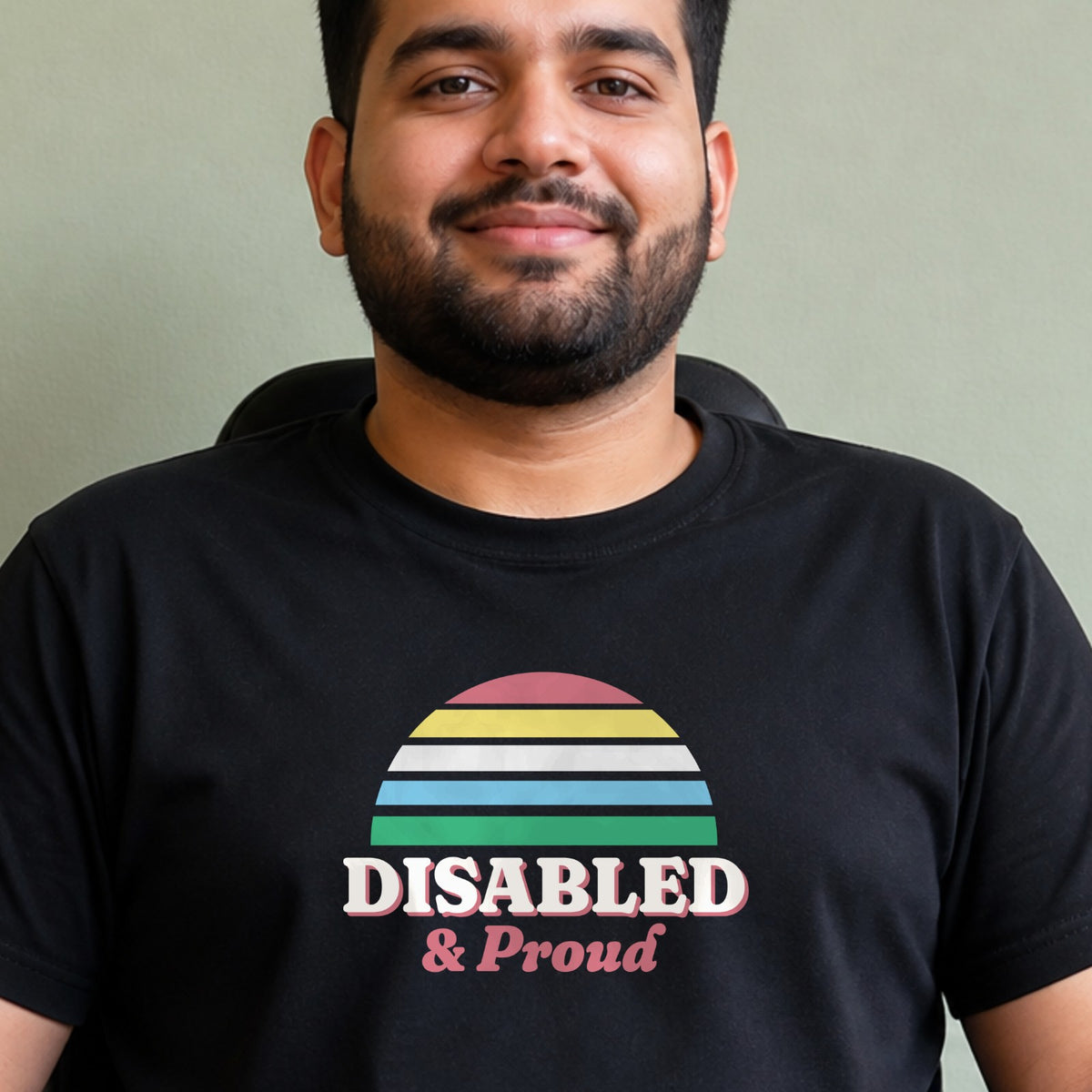 A man wears a black Disabled & Proud tee with a Disability Pride Flag-colored striped retro sun.
