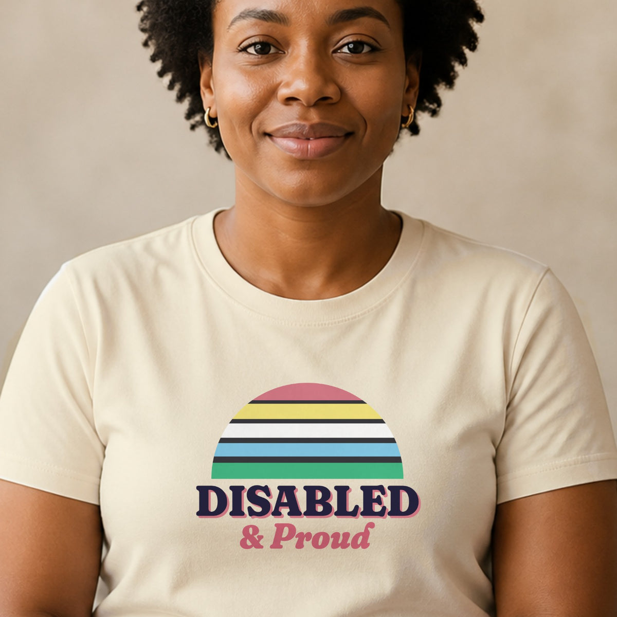 A woman wears a natural-colored Disabled & Proud tee with a Disability Pride Flag-colored striped retro sun.