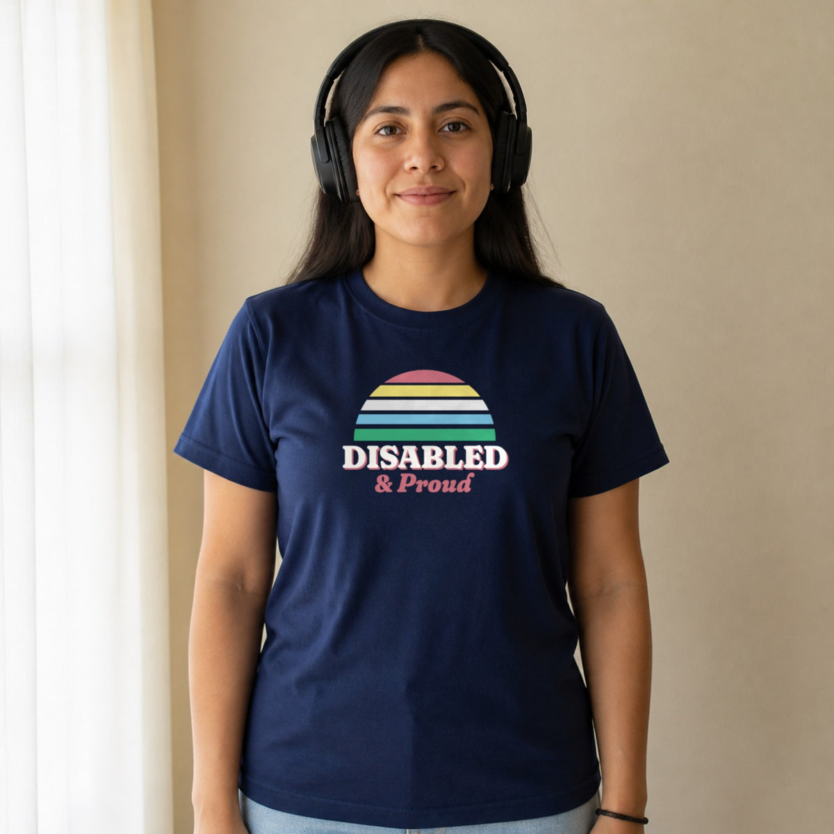 A woman in over-ear headphones wears a navy Disabled & Proud tee.