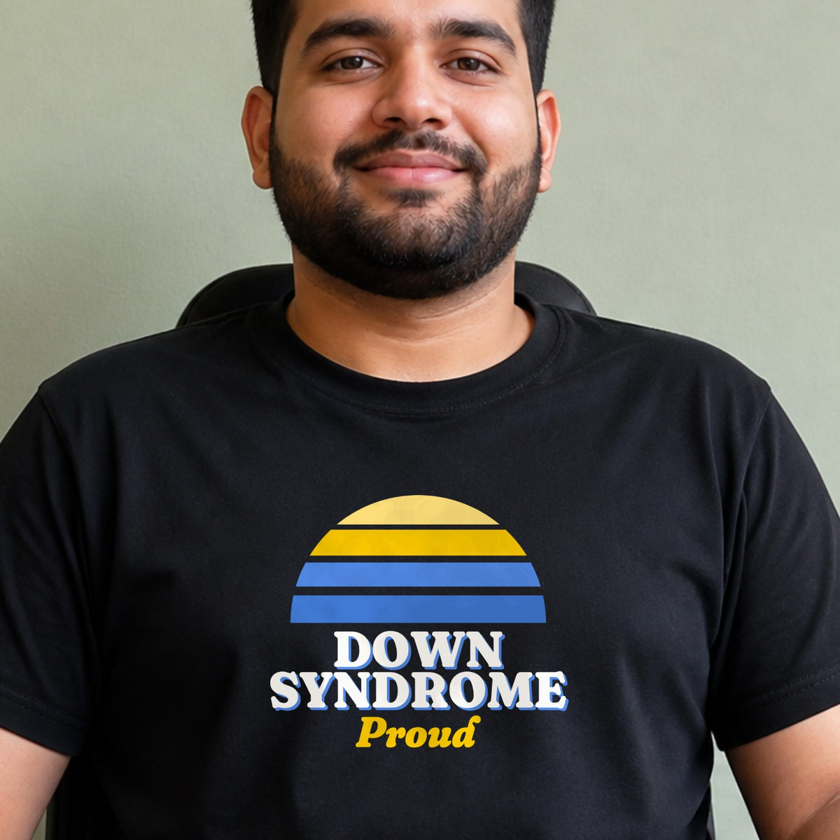 A man wears a black Down syndrome Proud tee with a blue and yellow striped retro sun.