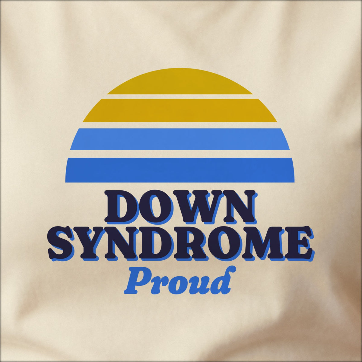 Close-up of the print on a natural tee: a striped half-sun in blue and yellow above bold DOWN SYNDROME lettering with “Proud” in script.