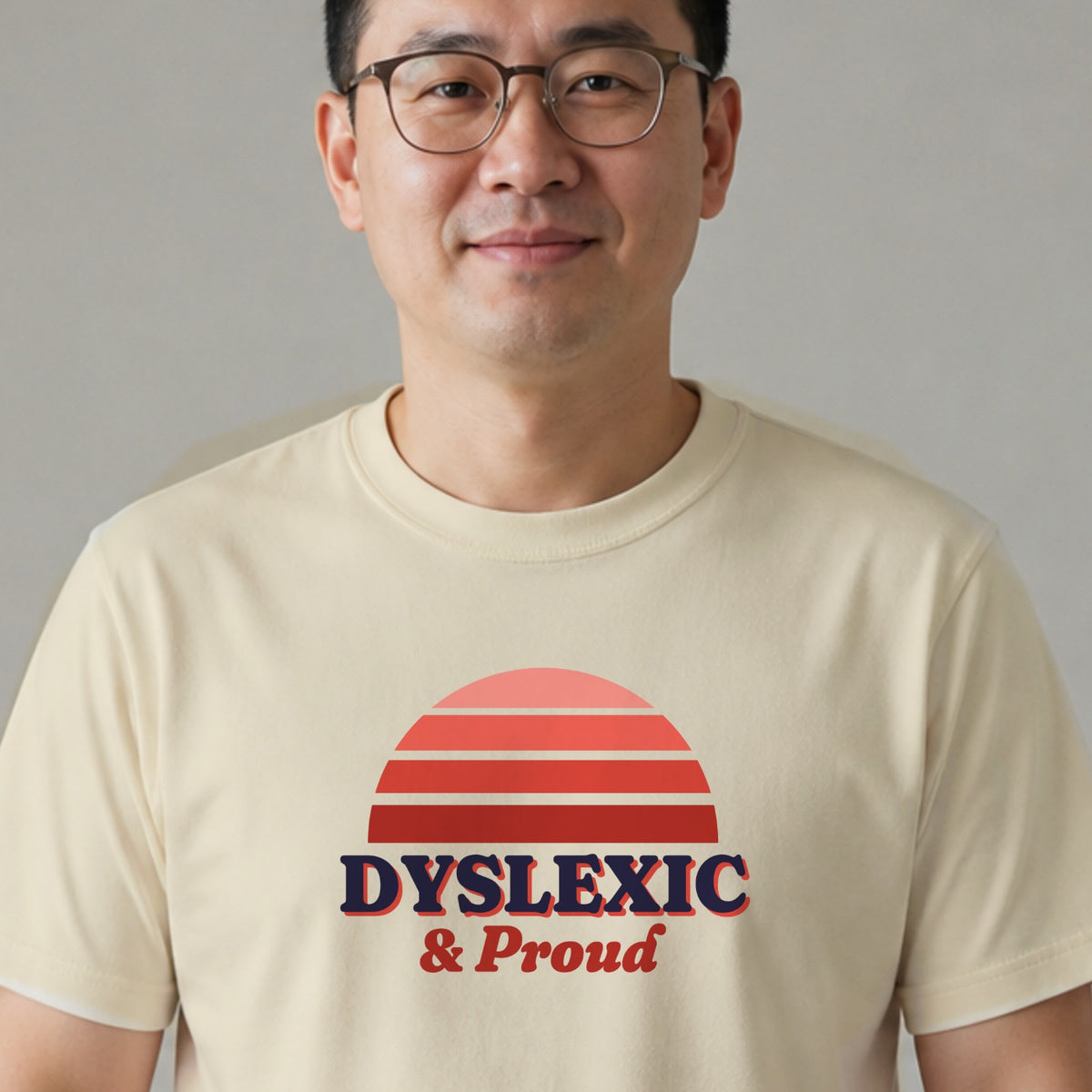 A man in glasses wears a natural-colored Dyslexic & Proud tee with a red striped retro sun.