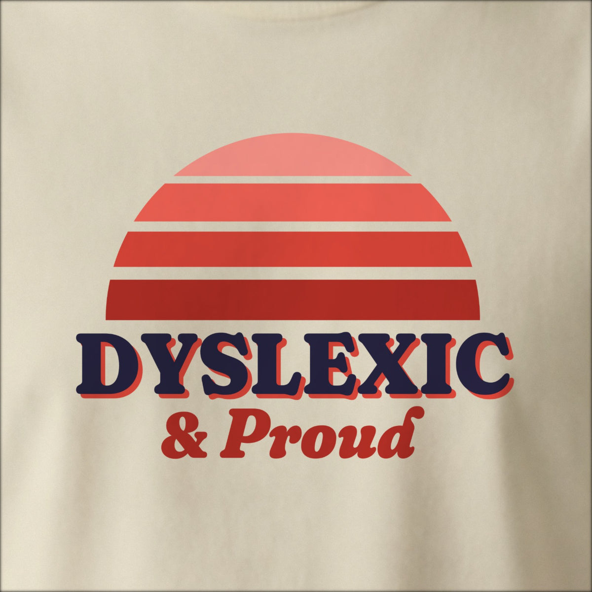 Close-up of the print on a natural tee: a striped half-sun in red above bold DYSLEXIC lettering with “& Proud” in script.