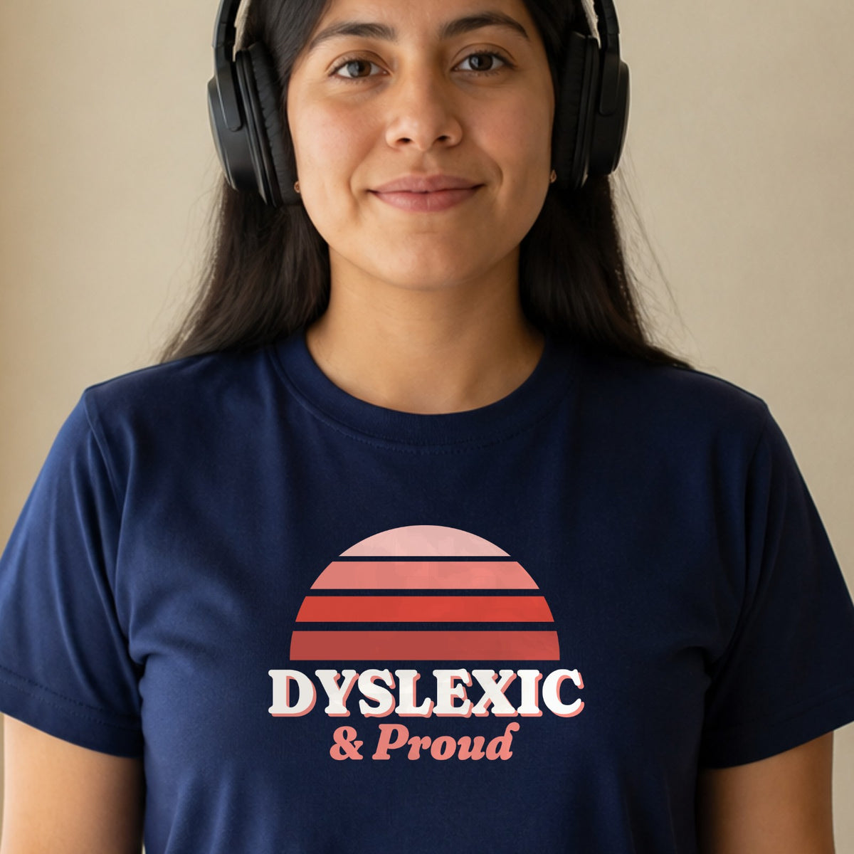 A woman in over-ear headphones wears a navy Dyslexic & Proud tee with a red striped retro sun.