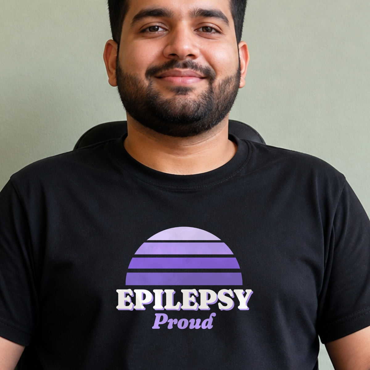 A man wears a black Epilepsy Proud tee with a purple striped retro sun.