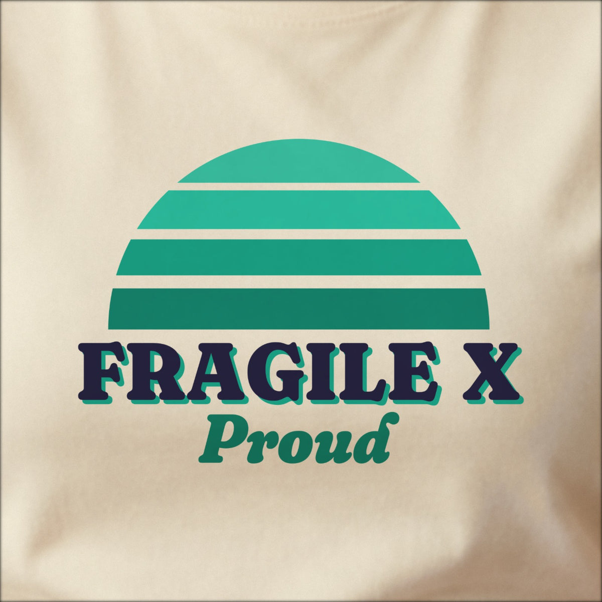 Close-up of the print on a natural tee: a striped half-sun in teal above bold FRAGILE X lettering with “Proud” in script.