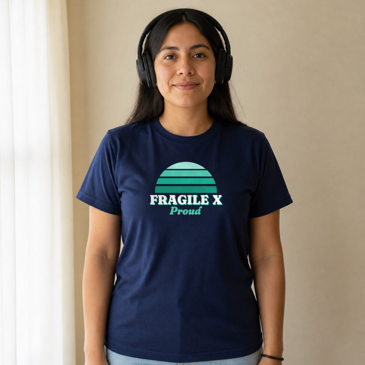 A woman in over-ear headphones wears a navy Fragile X Proud tee.