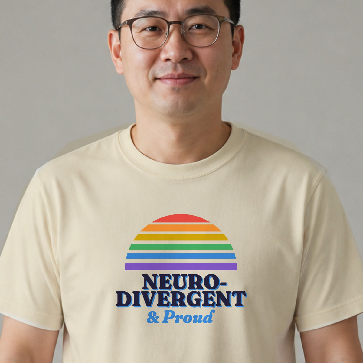 A man in glasses wears a natural-colored Neurodivergent & Proud tee with a rainbow striped retro sun.