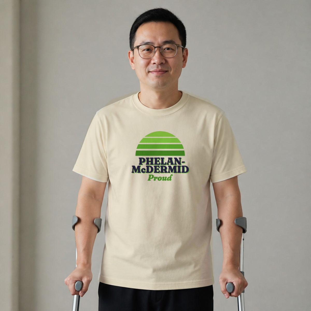A man standing with two forearm crutches wears a natural-colored Phelan-McDermid Proud tee.