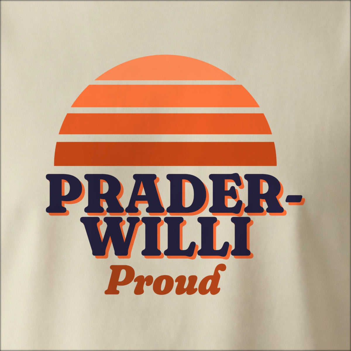 Close-up of the print on a natural tee: a striped half-sun in orange above bold PRADER-WILLI lettering with “Proud” in script.