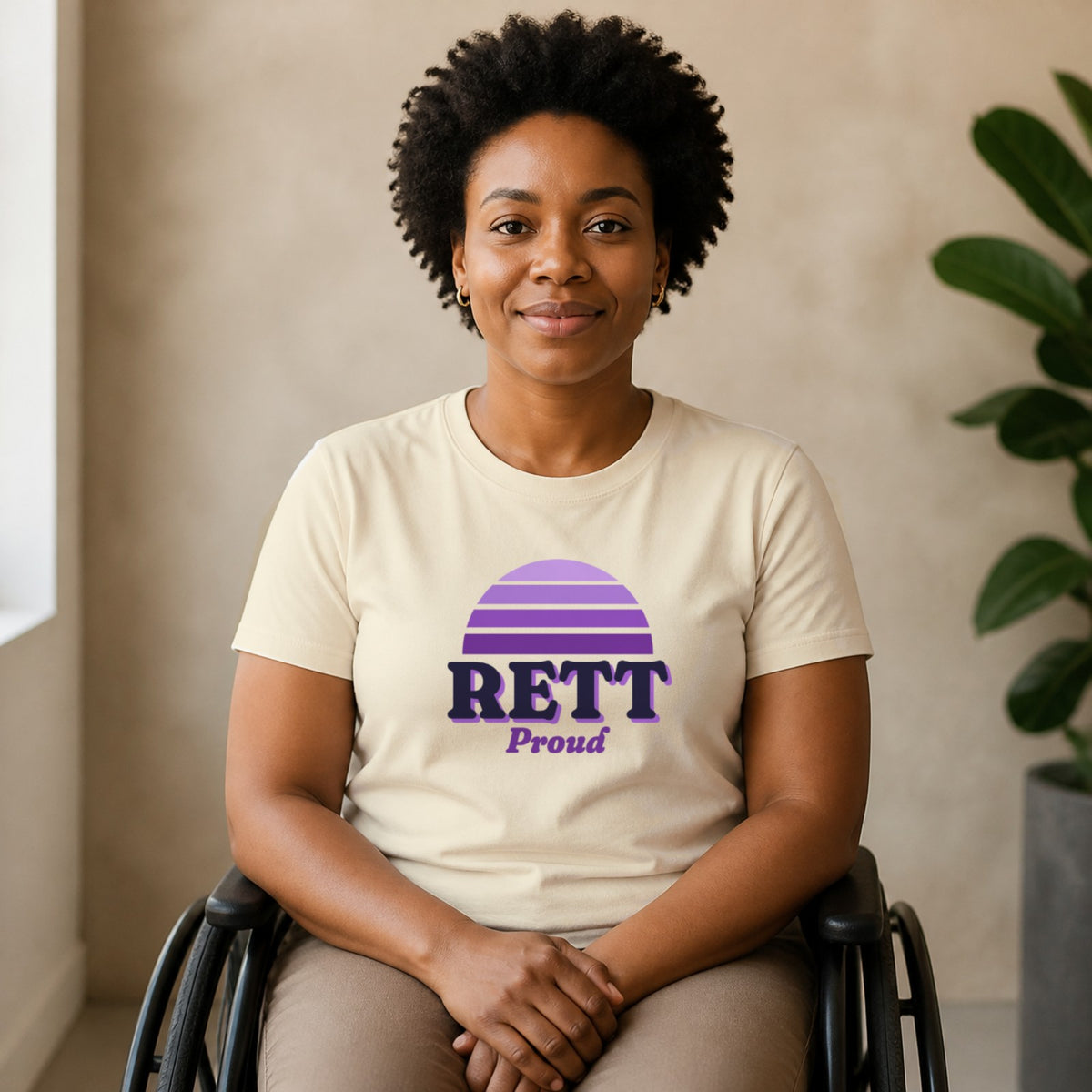 A woman seated in a wheelchair wears a natural-colored Rett Proud tee.