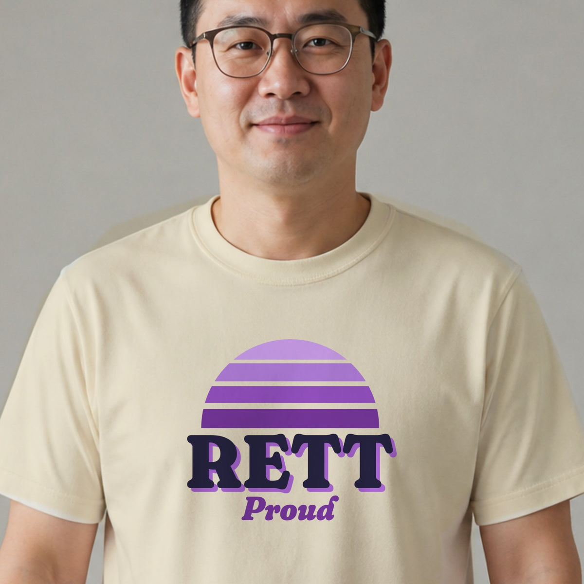 A man in glasses wears a natural-colored Rett Proud tee with a purple striped retro sun.