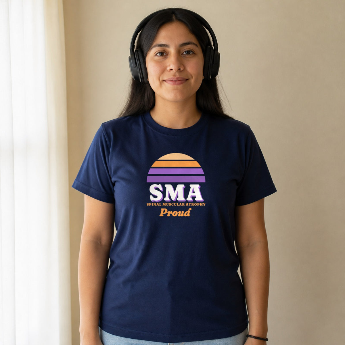 A woman in over-ear headphones wears a navy SMA Proud tee.