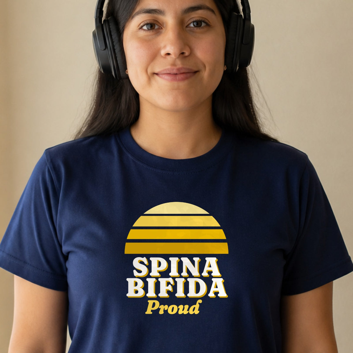 A woman in over-ear headphones wears a navy Spina Bifida Proud tee with a yellow striped retro sun.
