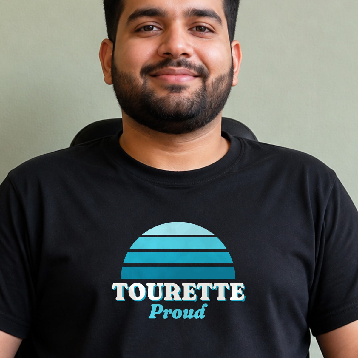 A man wears a black Tourette Proud tee with a teal striped retro sun.