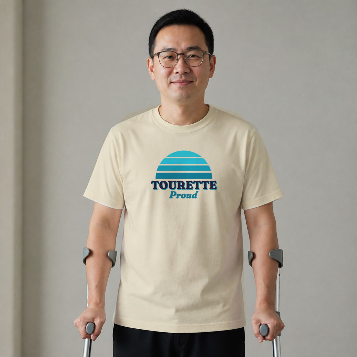A man standing with two forearm crutches wears a natural-colored Tourette Proud tee.