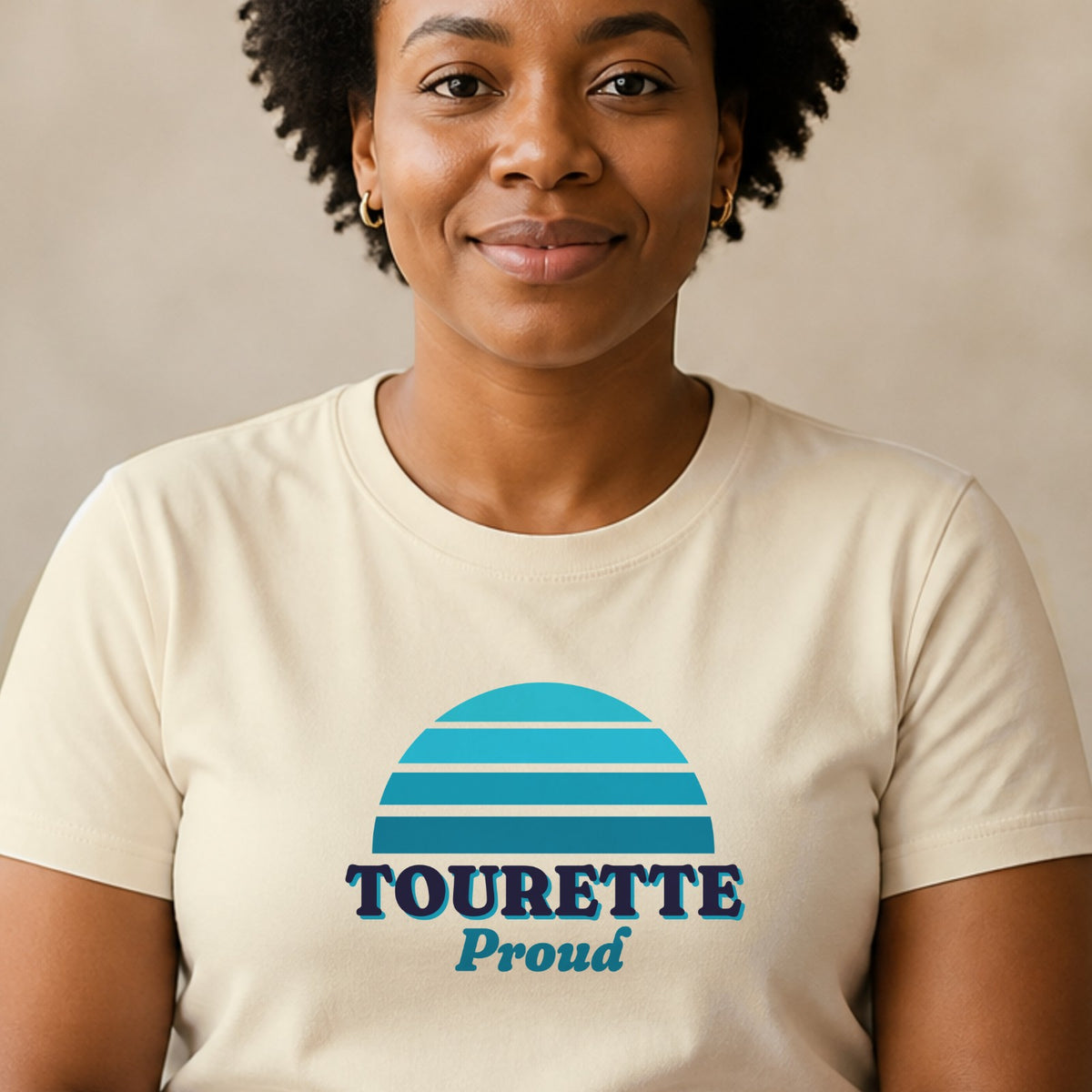 A woman wears a natural-colored Tourette Proud tee with a teal striped retro sun.